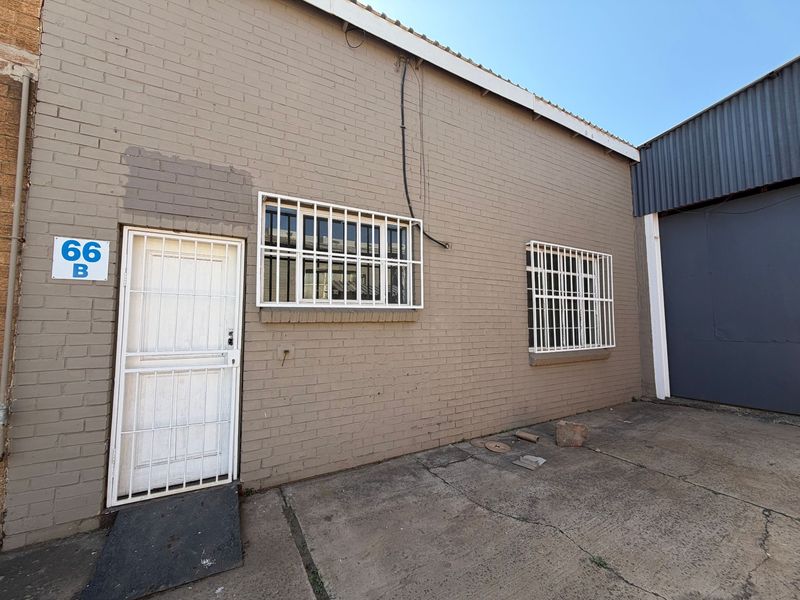 Rear exterior view of an industrial property featuring a brick facade, security-gated entrance, barred windows, and concrete paved yard area.