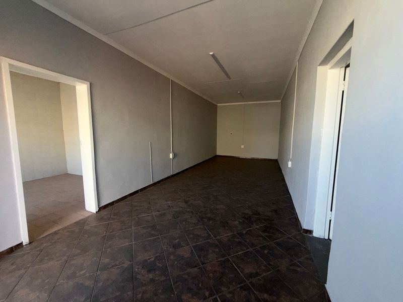 An empty, functional utility space featuring dark tiled flooring, neutral grey walls, and overhead fluorescent lighting, suitable for storage or office use.