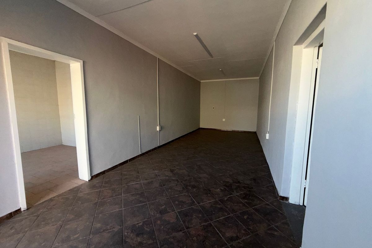 An empty, functional utility space featuring dark tiled flooring, neutral grey walls, and overhead fluorescent lighting, suitable for storage or office use.