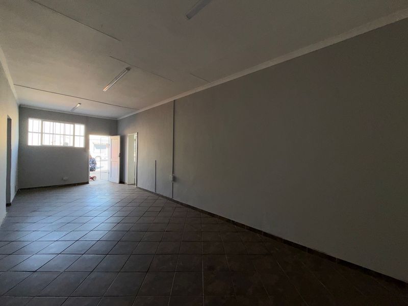 An empty, open-plan industrial utility space featuring tiled flooring, neutral walls, and functional overhead lighting, suitable for various commercial or storage applications.