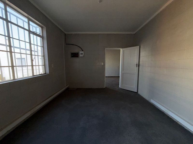 An empty utility space featuring tiled walls, security bars on the window, and an exposed electrical distribution board.