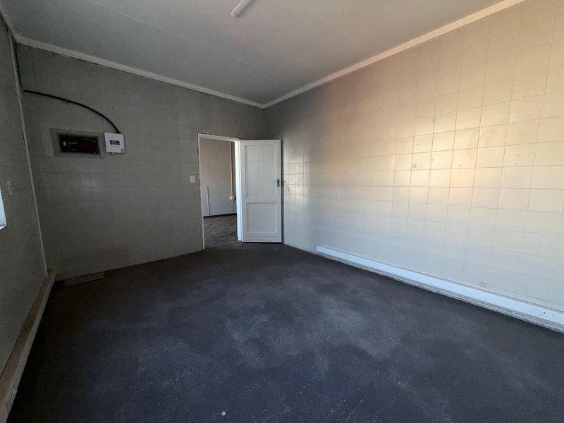 An empty utility space featuring tiled walls and an exposed electrical distribution board, suitable for storage or workshop use.