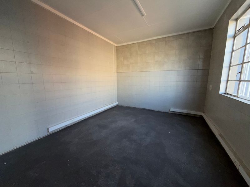 An empty industrial utility space featuring tiled walls, a steel-framed window, and basic overhead lighting, suitable for storage or workshop use.
