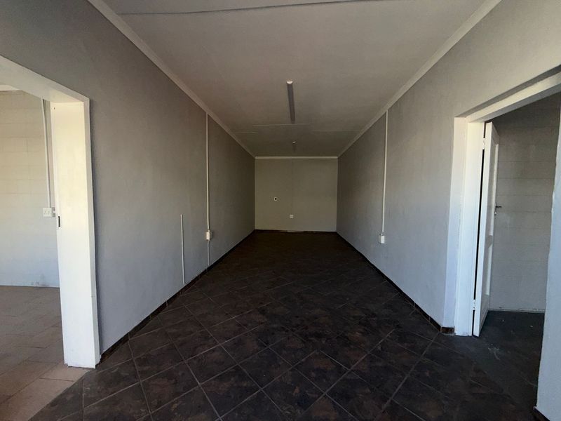 A clean, empty utility or storage space featuring dark tiled flooring, neutral grey walls, and surface-mounted electrical conduit.