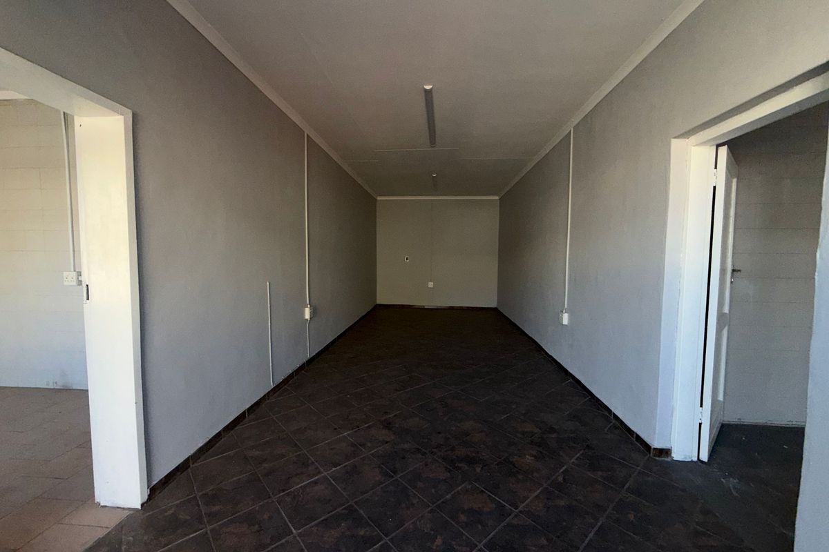 A clean, empty utility or storage space featuring dark tiled flooring, neutral grey walls, and surface-mounted electrical conduit.