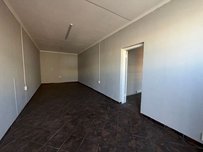 An empty, functional office space featuring tiled flooring, neutral walls, and overhead fluorescent lighting, suitable for various commercial or industrial business applications.