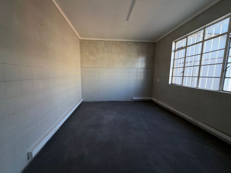 An empty, industrial-style utility space featuring tiled walls, a steel-framed window with security bars, and a concrete floor.