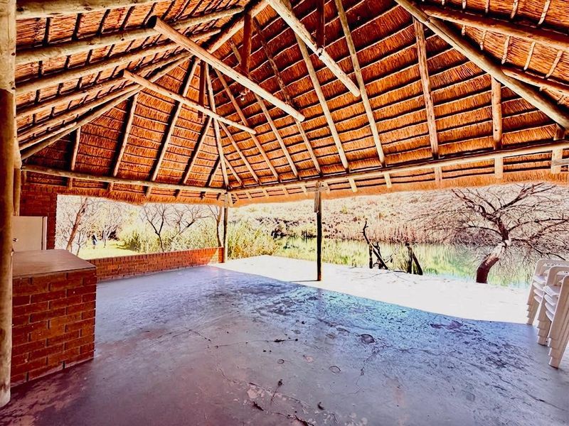 Spacious outdoor thatched patio area featuring a built-in brick counter, exposed timber roof structure, and scenic views of the surrounding landscape.