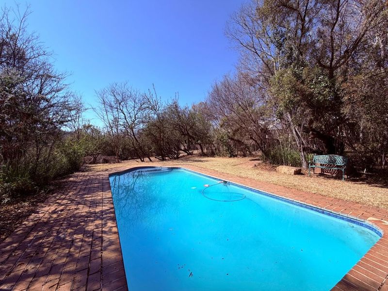 A private outdoor swimming pool area featuring brick paving and surrounding mature trees in a natural farm setting.