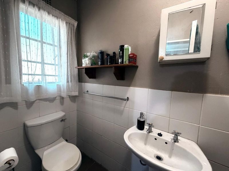 A functional bathroom featuring a pedestal basin, toilet, and wall-mounted medicine cabinet with tiled splashback finishes.