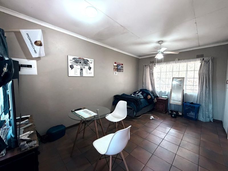 A bedroom featuring tiled flooring, a ceiling fan, and security burglar bars on the window, with visible signs of ceiling water damage.