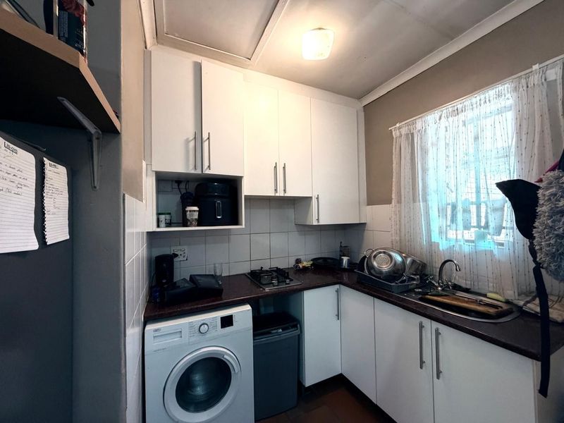 Compact kitchen featuring white cabinetry, dark countertops, a gas hob, and integrated laundry plumbing, offering a functional workspace.