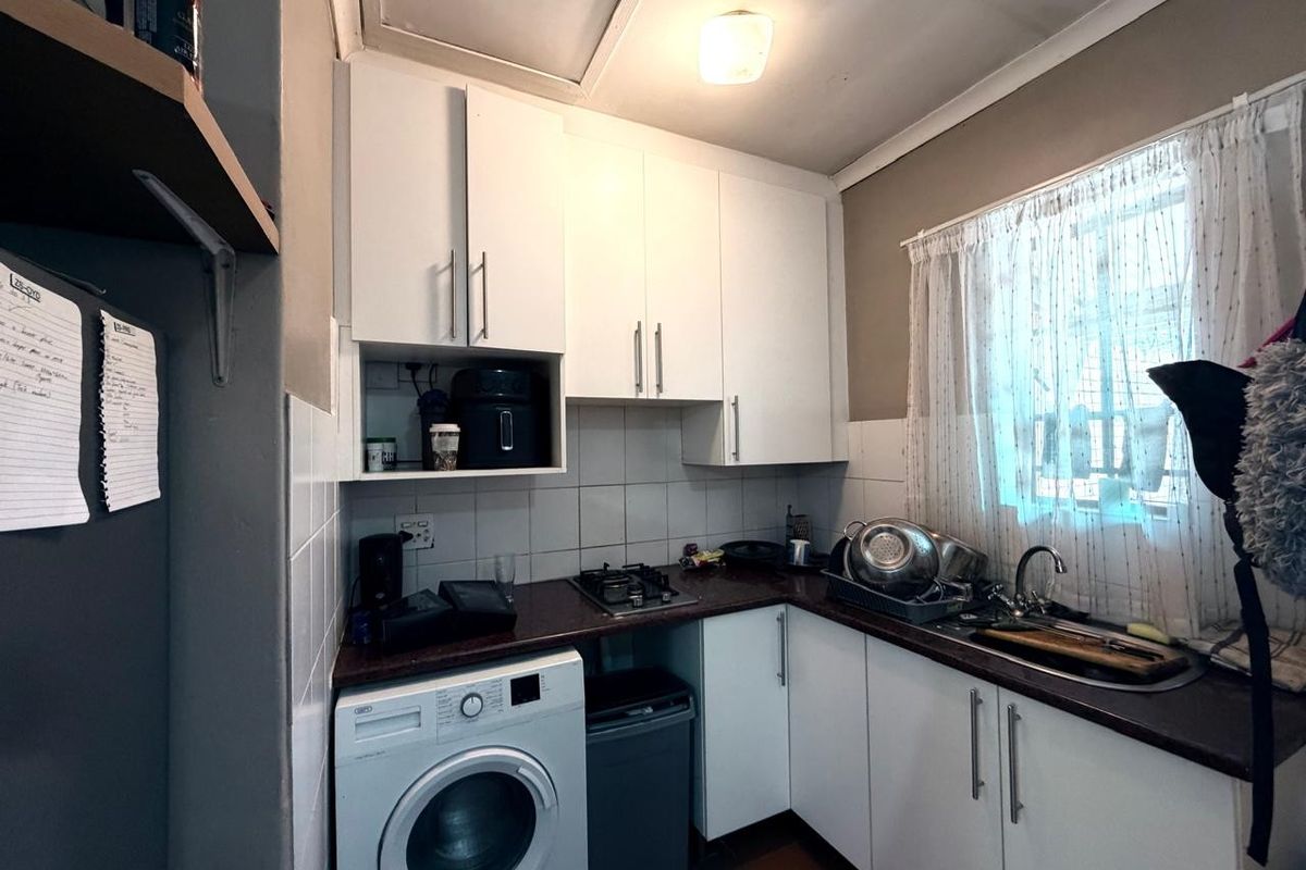 Compact kitchen featuring white cabinetry, dark countertops, a gas hob, and integrated laundry plumbing, offering a functional workspace.