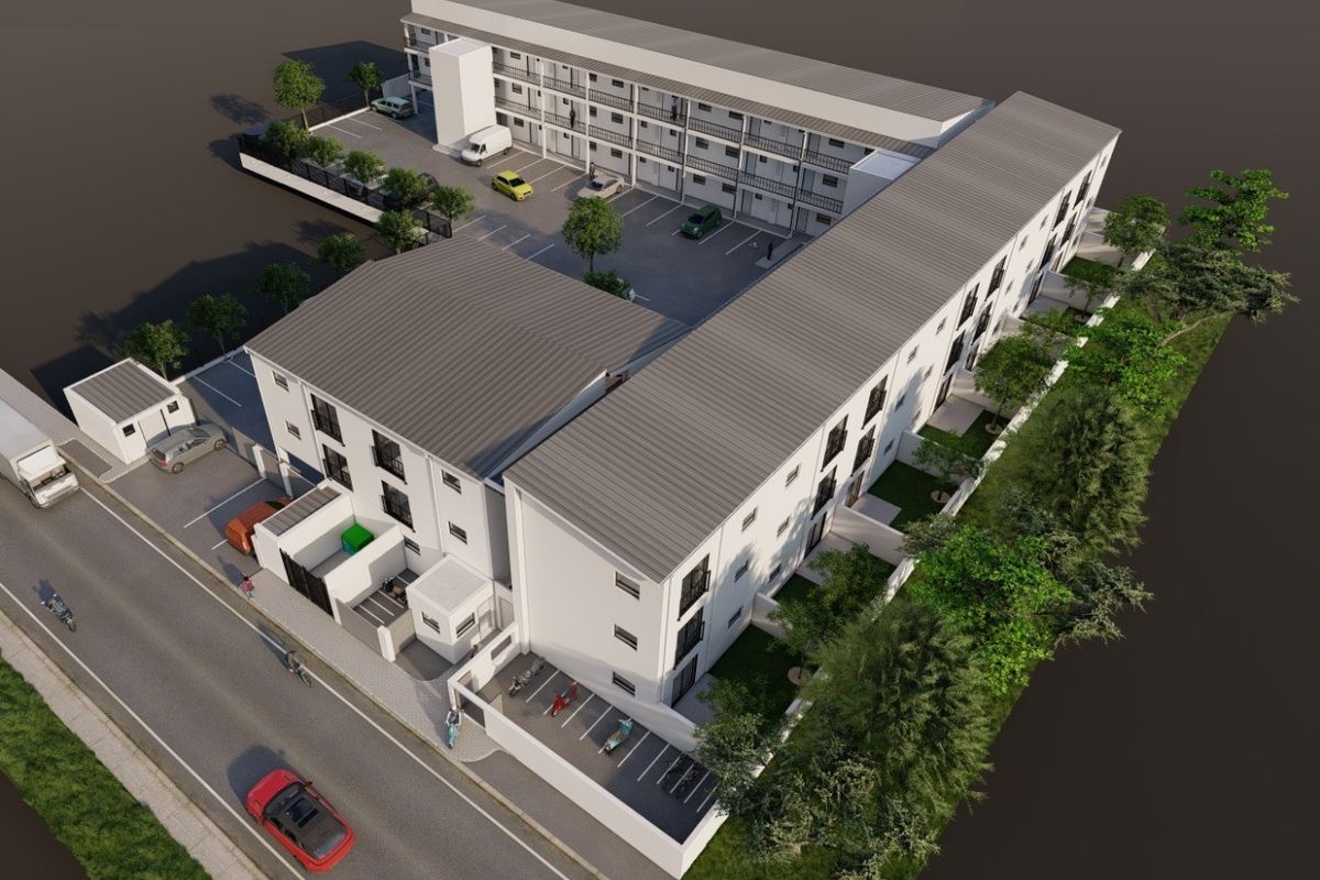 Aerial view of a modern multi-story residential complex featuring paved parking, landscaped grounds, and secure perimeter fencing.
