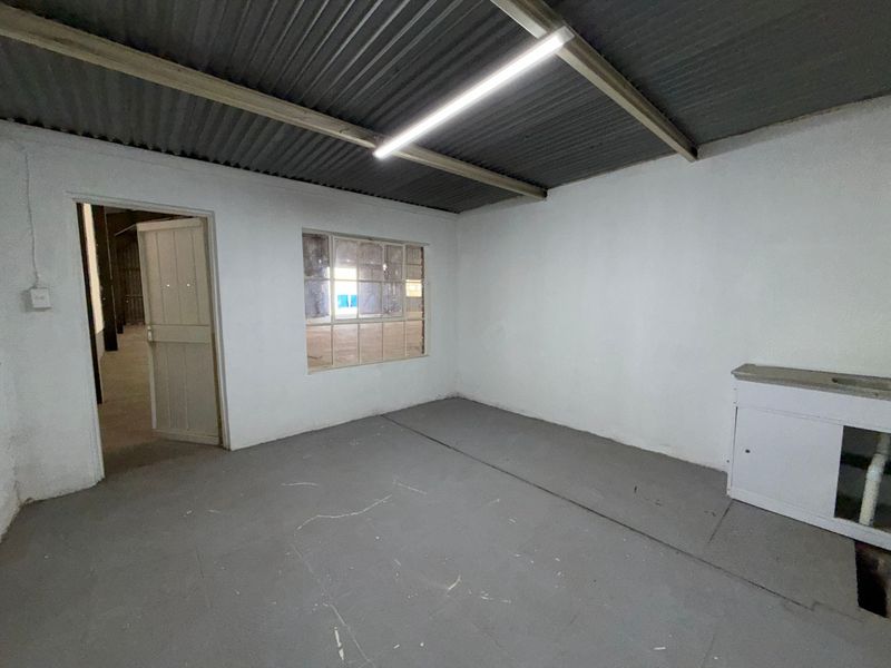 A functional utility space featuring a corrugated metal ceiling, fluorescent lighting, and a built-in sink unit, suitable for industrial or workshop use.