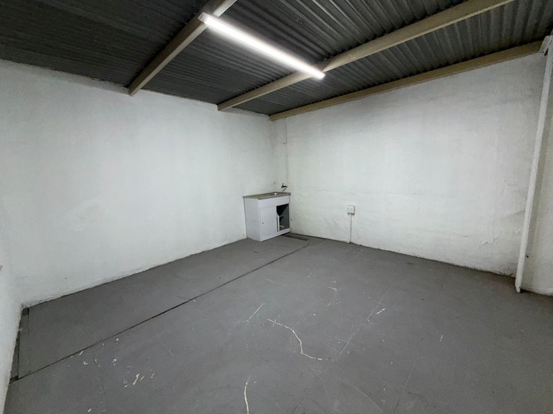 An empty industrial utility space featuring a corrugated metal roof, fluorescent lighting, and a small built-in sink cabinet.