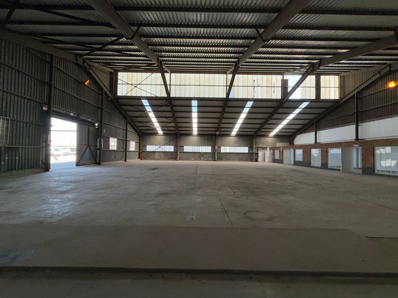 Spacious industrial warehouse featuring high ceilings with steel trusses, concrete flooring, and ample natural light through translucent roof panels and side windows.
