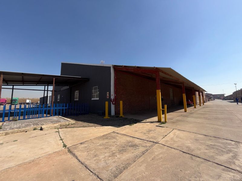 Industrial warehouse exterior featuring corrugated metal and brick construction with a large concrete apron and covered loading area.