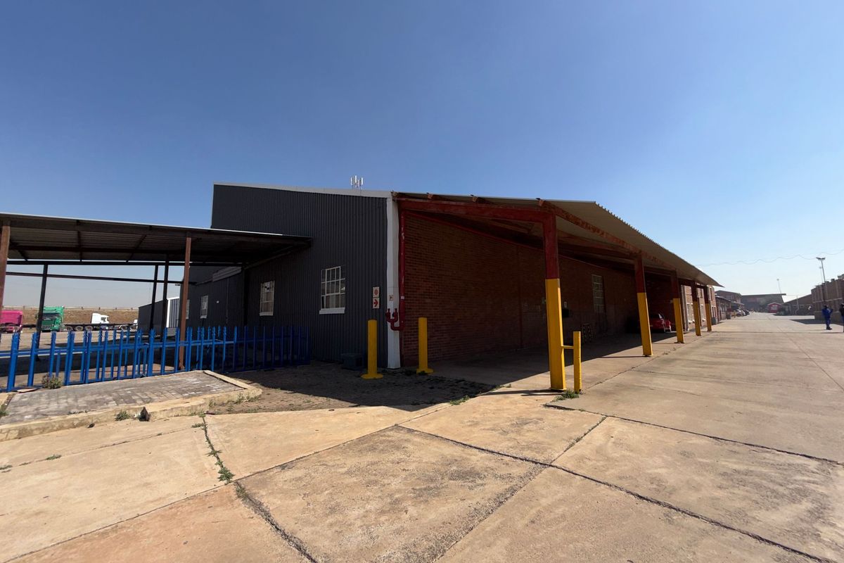 Industrial warehouse exterior featuring corrugated metal and brick construction with a large concrete apron and covered loading area.