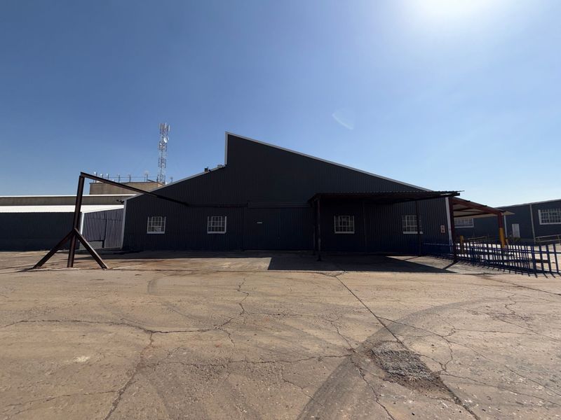 Rear view of an industrial warehouse building featuring corrugated metal cladding, a steel canopy, and a large asphalt yard area.