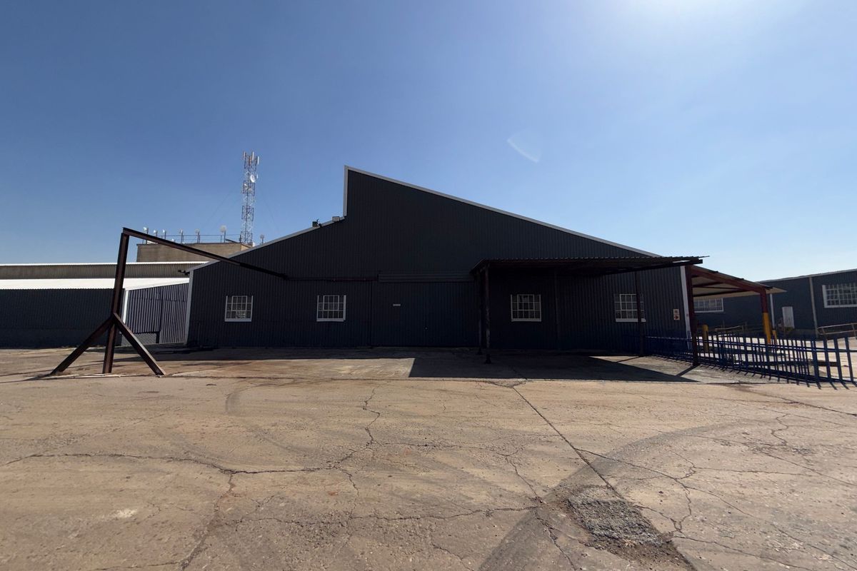 Rear view of an industrial warehouse building featuring corrugated metal cladding, a steel canopy, and a large asphalt yard area.