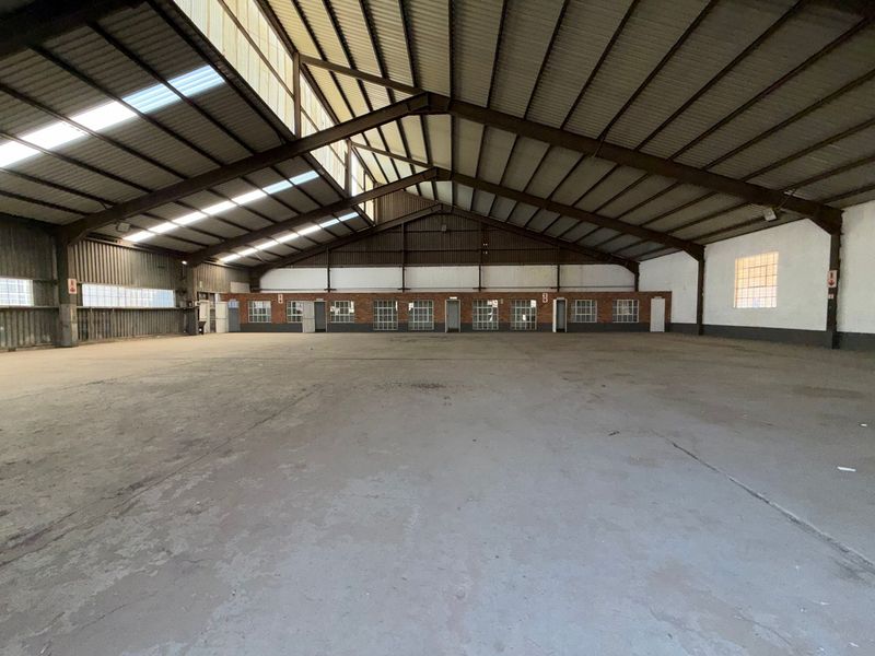 Spacious industrial warehouse featuring a high-clearance steel portal frame, concrete flooring, and ample natural light through translucent roof panels and perimeter windows.