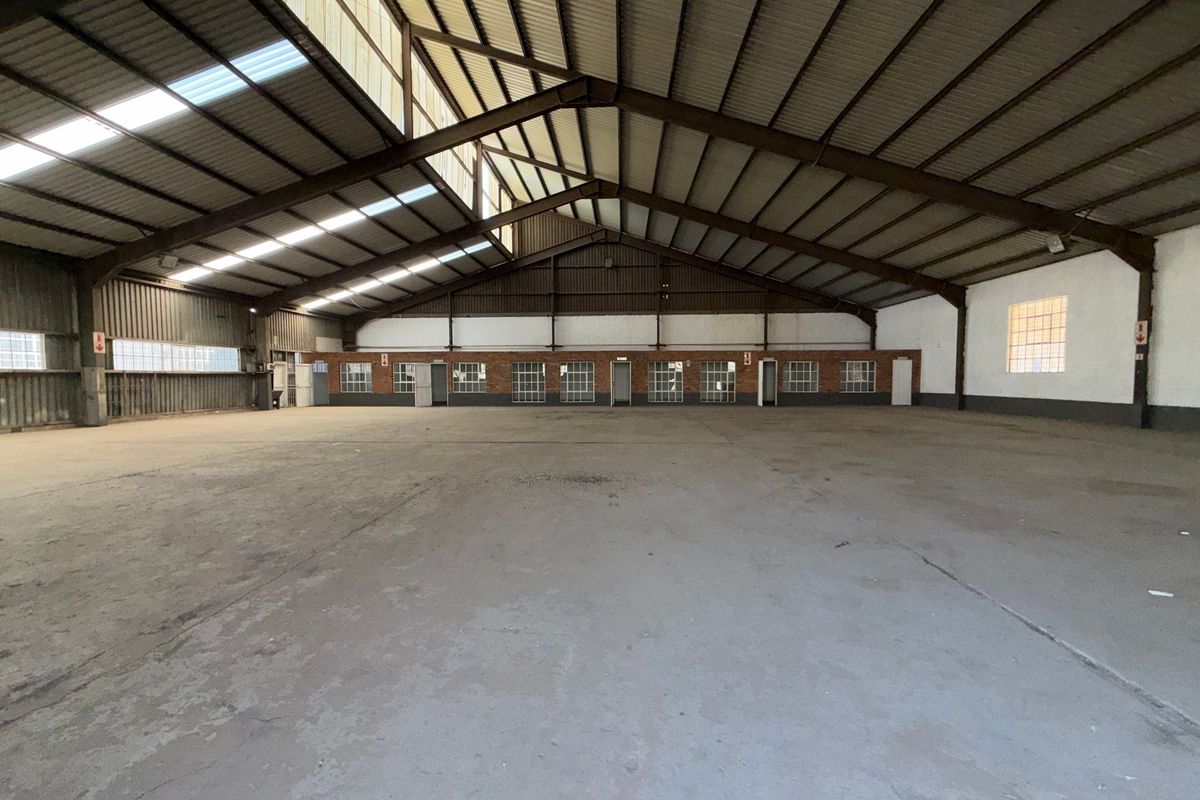 Spacious industrial warehouse featuring a high-clearance steel portal frame, concrete flooring, and ample natural light through translucent roof panels and perimeter windows.