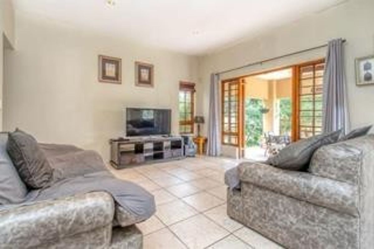Spacious living room featuring tiled flooring, recessed lighting, and large timber-framed glass doors providing seamless access to the outdoor patio area.