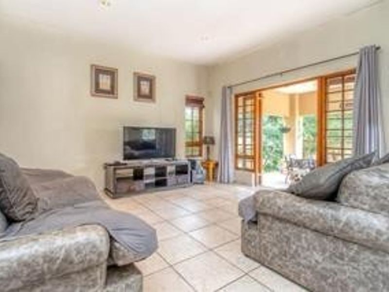 Spacious living room featuring tiled flooring, recessed lighting, and large timber-framed glass doors providing seamless access to the outdoor patio area.