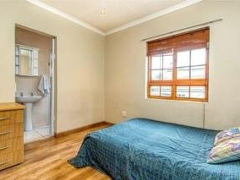 A bedroom featuring laminate flooring, a wooden window frame, and an attached en-suite bathroom with a pedestal basin.