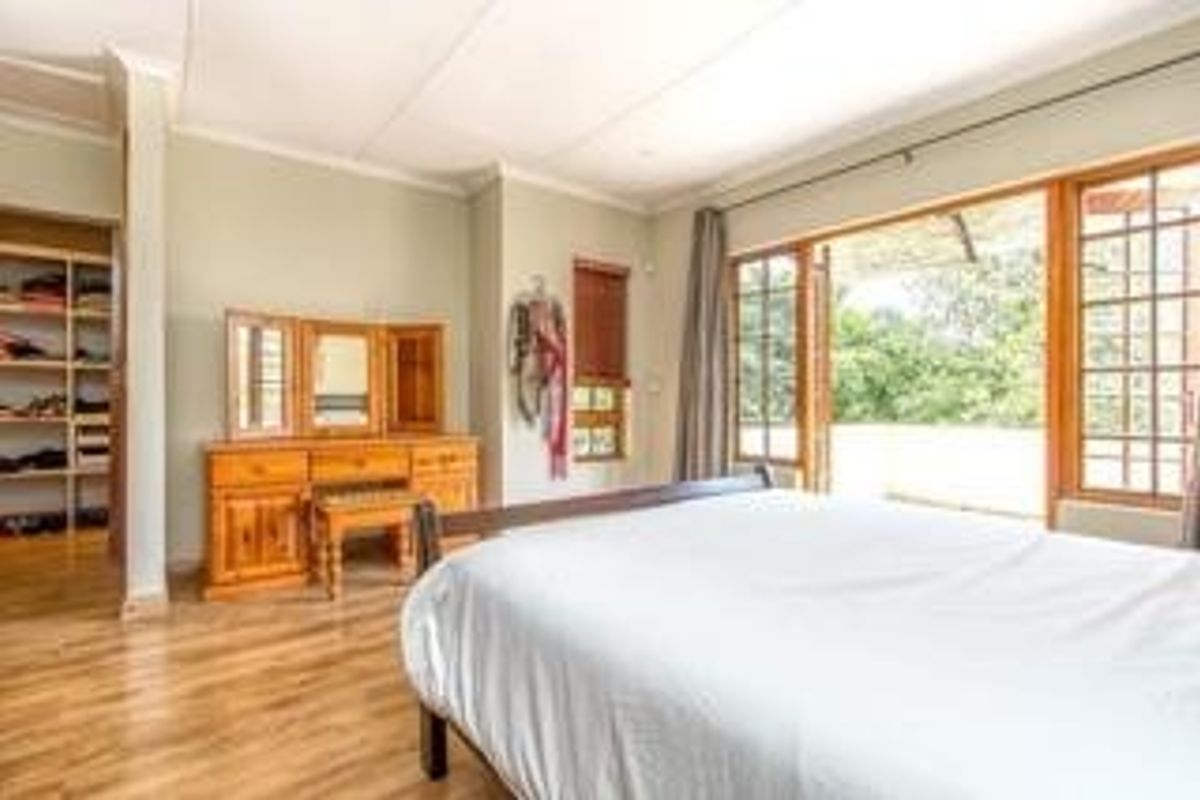 Spacious bedroom featuring wooden flooring, built-in shelving, and large wooden french doors opening onto an outdoor area.