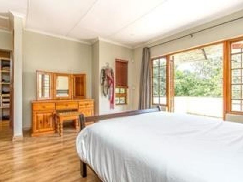 Spacious bedroom featuring wooden flooring, built-in shelving, and large wooden french doors opening onto an outdoor area.