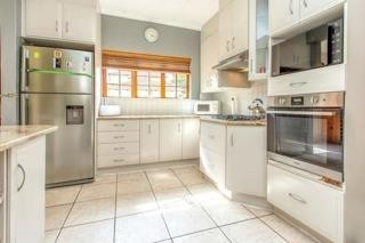 A functional kitchen featuring white cabinetry, tiled flooring, a built-in oven, microwave, and extractor fan, offering a clean and practical workspace.