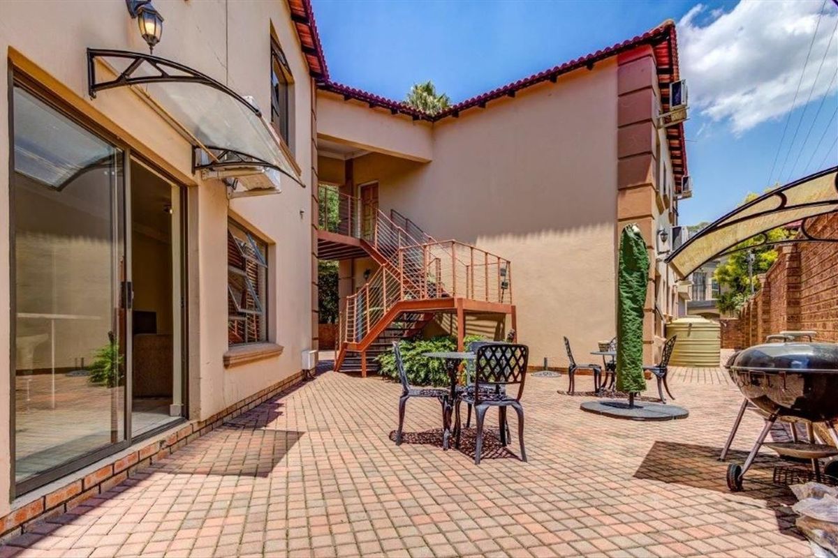 A paved rear courtyard featuring a metal staircase, sliding door access, and a brick boundary wall, providing a functional outdoor entertainment space.