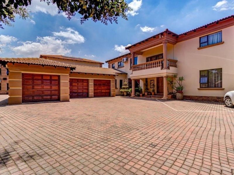Spacious front exterior featuring a large paved driveway, triple garage with wooden doors, and a multi-story facade with a covered balcony.