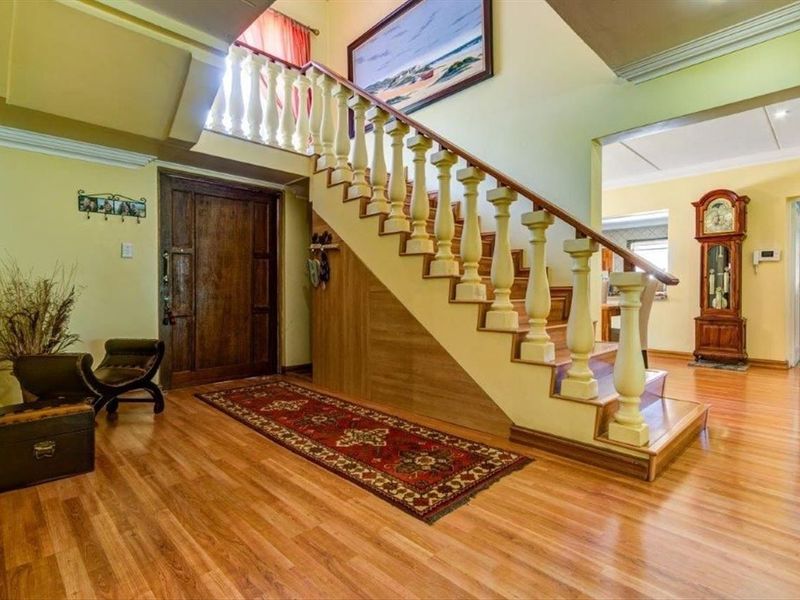 Spacious entrance hall featuring a prominent wooden staircase with balustrade, warm laminate flooring, and a solid wood front door.