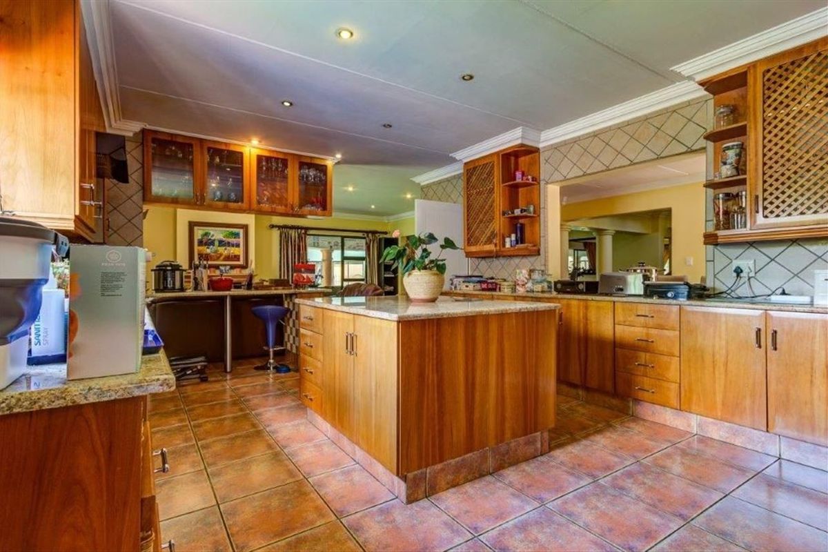 Spacious kitchen featuring warm wooden cabinetry, granite countertops, a central island, and tiled flooring, offering a functional layout with ample storage space.