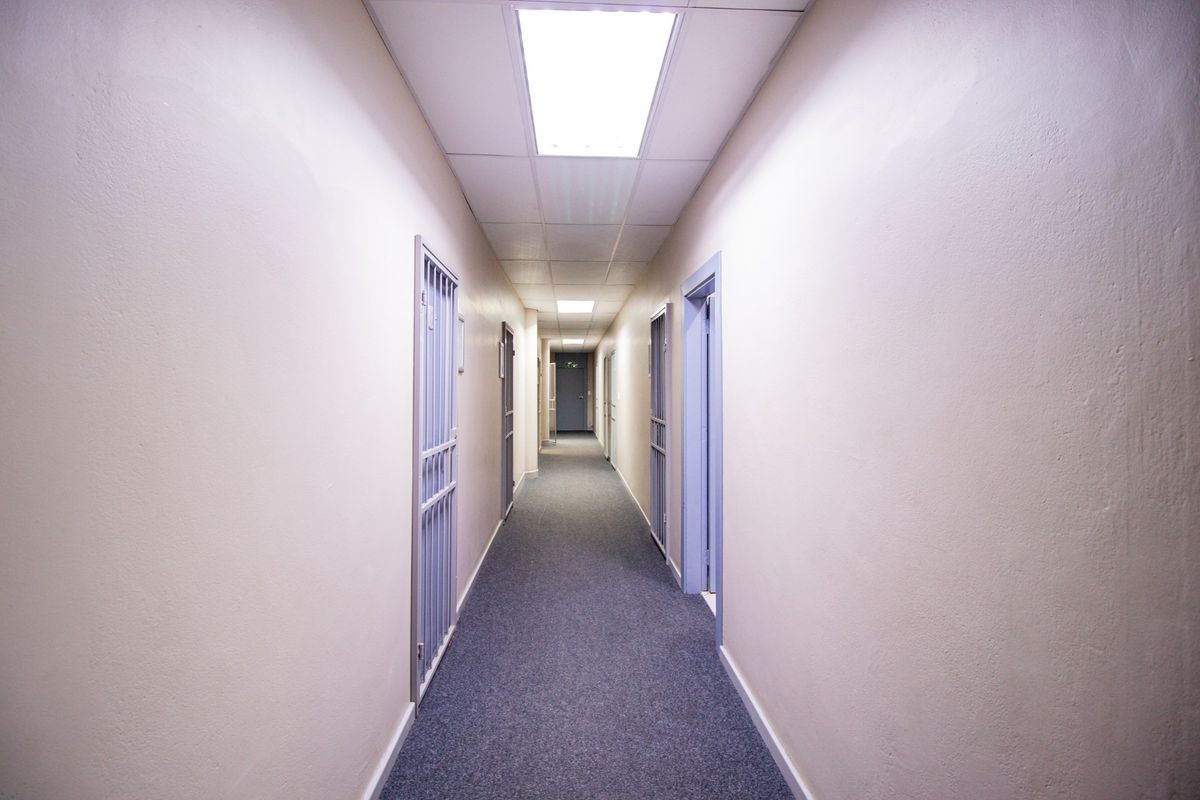 A clean, functional commercial hallway featuring carpeted flooring, suspended ceiling tiles with recessed lighting, and multiple security gates leading to individual office spaces.
