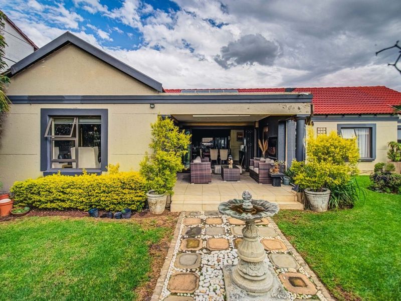 Rear view of the property featuring a covered patio, landscaped garden with a stone pathway, and solar panels installed on the tiled roof.