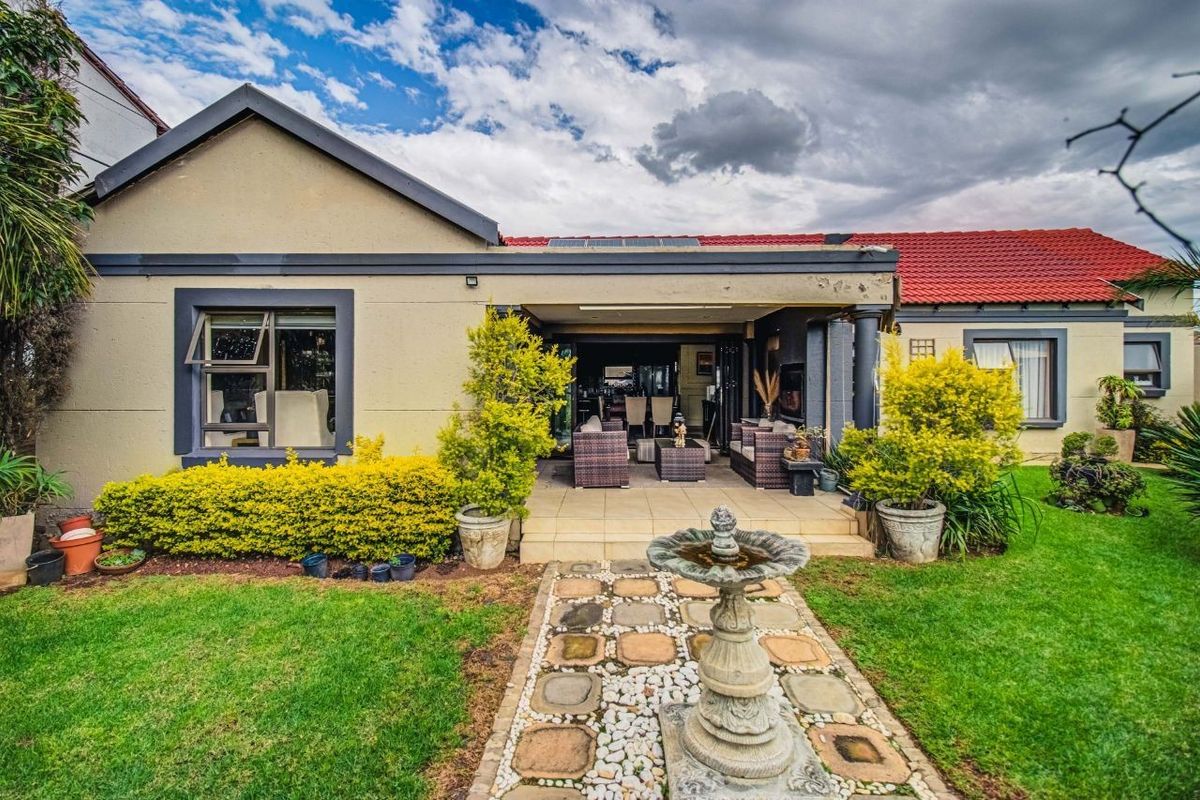 Rear view of the property featuring a covered patio, landscaped garden with a stone pathway, and solar panels installed on the tiled roof.