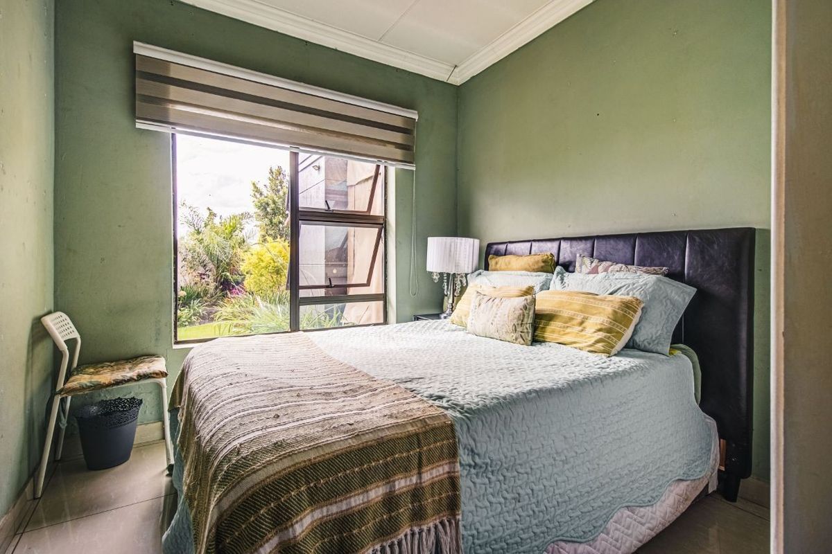 A bedroom featuring tiled flooring, green painted walls, and a large window with a roller blind overlooking the garden.
