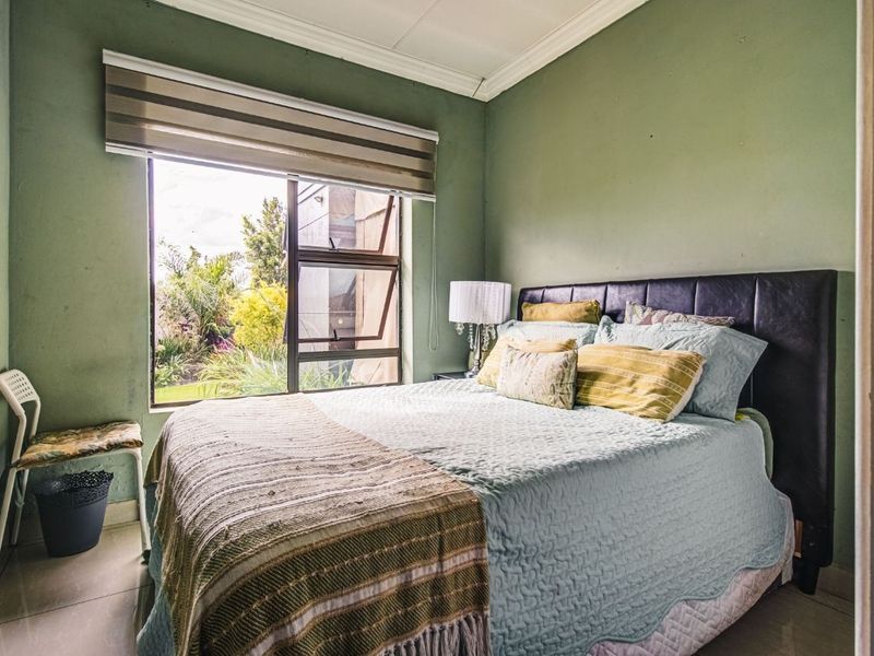 A bedroom featuring tiled flooring, green painted walls, and a large window with a roller blind overlooking the garden.
