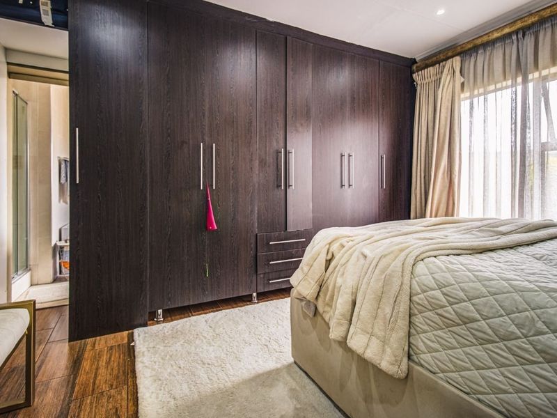 A well-maintained bedroom featuring extensive dark wood built-in cupboards, warm laminate flooring, and neutral finishes with access to an en-suite bathroom.