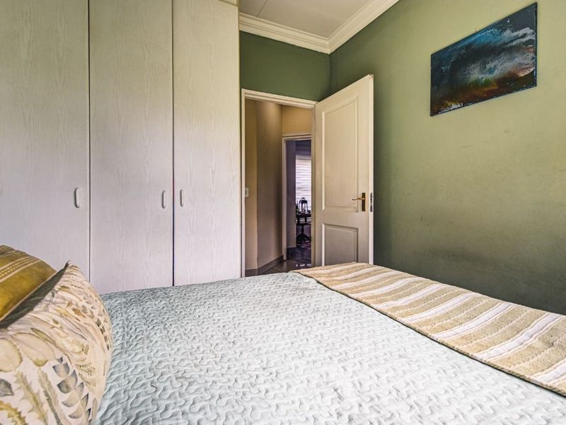 A bedroom featuring built-in cupboards and green painted walls, with a view through the doorway into the adjacent hallway.