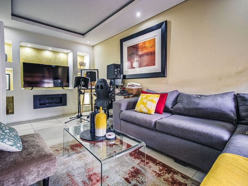 A comfortable living room featuring a built-in media wall with recessed lighting, tiled flooring, and a modern cove ceiling design.