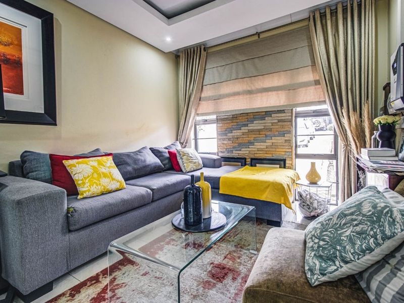 A cozy living room featuring a stone veneer accent wall, recessed ceiling lighting, and neutral tiled flooring.