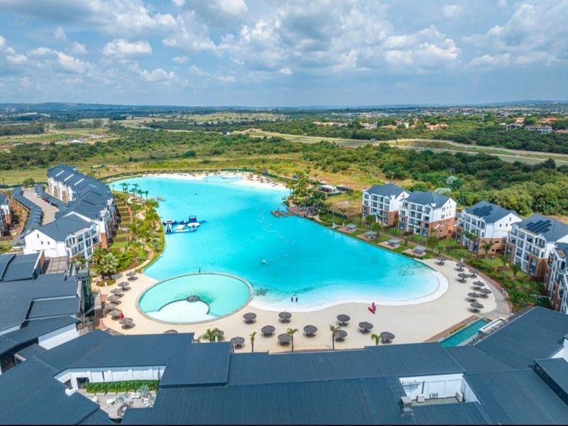 Aerial view of a modern apartment complex featuring a large central swimming lagoon, landscaped surroundings, and multi-story residential buildings.