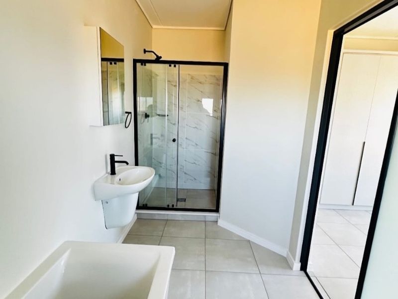 Modern bathroom featuring a walk-in shower with black frame, wall-mounted basin, and a bathtub with neutral floor tiling.