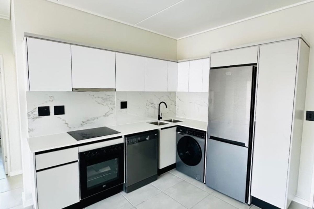 Modern kitchen featuring white cabinetry, marble-look splashback, integrated appliances, and sleek track lighting, set against neutral tiled flooring.