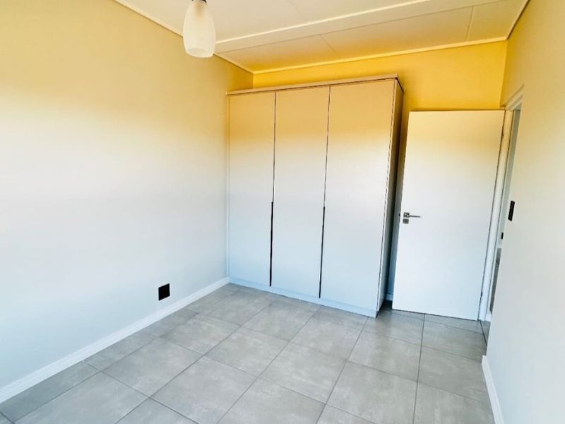 A clean, empty bedroom featuring neutral tiled flooring, a built-in wardrobe, and a modern pendant light fixture.